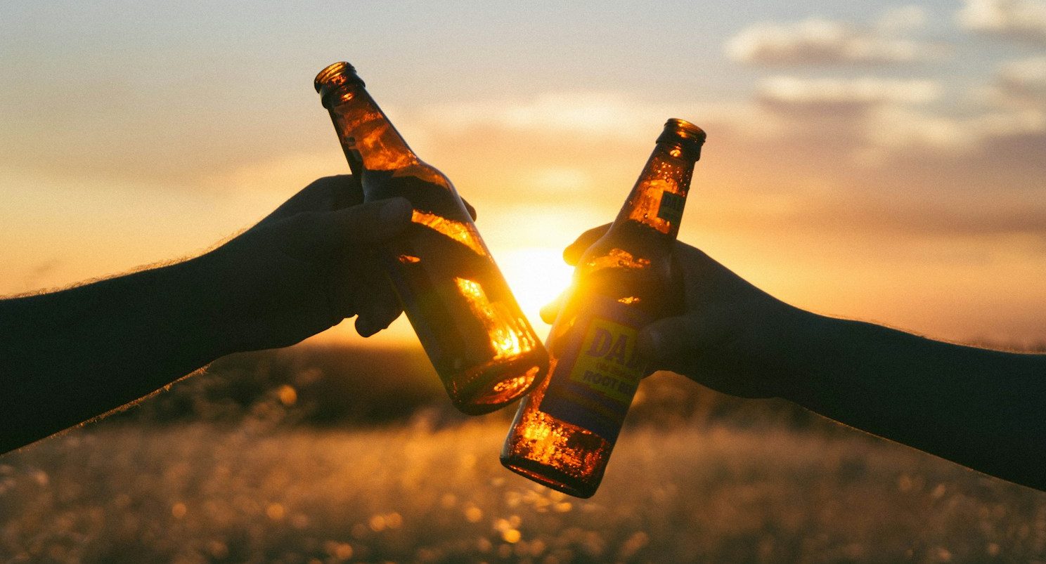 photography of person holding glass bottles during sunset